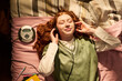 © pressmaster - Teenager girl lying on bed, listening through headphones beside portable CD player, relaxing during study break and expressing youth leisure. Top view, ideal for teen lifestyle campaigns