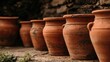 © pvl0707 - Rustic terracotta clay pots line up against a weathered stone wall in a dimly lit setting with dusty stone floor
