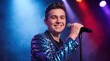 © IbragimovN - Energetic young performer in sparkling jacket singing on stage with colorful lights for event promotion and entertainment design