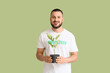 © Pixel-Shot - Smiling young man in a volunteer t-shirt holding a potted plant, environmental conservation and green living