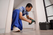 © Pixel-Shot - Male worker with electric drill installing door hinge at home