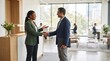 © GALKI - Two business professionals, a man and a woman of diverse ethnicity, shake hands and smile warmly in a modern office setting, symbolizing a successful meeting or partnership.