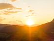 © AmazingAerialAgency - Aerial view of Fiemme Valley at sunset with golden light illuminating the rolling hills and mountain peaks in Trentino-Alto Adige, Italy.