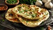 © Nasreen - Indian naan bread with fresh herbs and garlic seasoning served on plate, authentic homemade flatbread, traditional indian cuisine, rustic bakery food, soft golden garlic naan, delicious side dish for