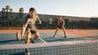 © Anucha - Two people playing an intense game of pickleball on an outdoor court during sunset.