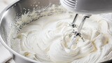 Whipped cream being mixed in a stainless steel bowl with mixer  