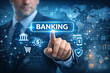 © Natalia - A corporate businessman in suit and tie pointing at the word 'BANKING' on a holographic interface representing digital banking and finance technology.