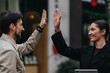 © qunica.com - Two coworkers share a high five while smiling at each other outdoors. A friendly urban moment showing teamwork and mutual celebration.