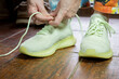 © Chris - Person is tying shoelaces on green sneakers indoors on a wooden floor during the day