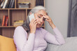 © Prostock-studio - Worried Elderly Hispanic Woman Speaking On Phone With A Concerned Expression, Sitting On Couch At Home. Emotion Reflects Stress And Anxiety, Bringing Attention To Mental Health And Wellbeing Concept.