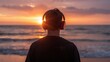 © VolumeThings - Back view of a young man wearing large headphones by the ocean at sunset, enjoying music with his back facing the camera.