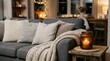 © kinkin - Cozy living room interior with dark grey sofa, cushions, warm throw blanket, and burning candle on wooden side table in evening