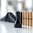 © Mr. Orsetto - Black chess pawn standing strong in front of falling dominoes representing resilience and strategic defense in challenging situations on white surface