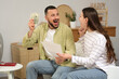 © Pixel-Shot - Happy young couple with refund form and money sitting on sofa at home