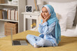 © Pixel-Shot - Little Muslim girl in hijab sitting on bed with modern laptop at home