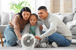 © Pixel-Shot - Frozen family warming hands near electric fan heater at home