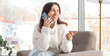 © Pixel-Shot - Smiling young woman talking on a mobile phone while relaxing in a comfortable armchair at home, communication and connection