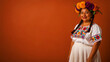 © DURAND HUGO VICTOR - Latina woman in traditional embroidered clothing wearing a colorful flower crown. Smiling person posing against a solid orange background with copy space. Cultural heritage celebration theme.