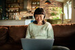 © Davor - Smiling woman using laptop on sofa at home
