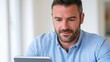 © ISVO - Male individual with short dark hair and beard using a tablet device while seated indoors, focused on the screen in a well-lit environment