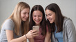 © ChaoticDesignStudio - Teenage girls laughing while looking at smartphone screen together. Group of friends watching funny video or social media content on mobile device.
