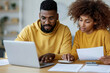 © lashkhidzetim - Young couple reviews finances together at home. They focus intently on laptop and papers. Warm yellow tones add cozy atmosphere. Suggests teamwork, budgeting, or financial planning