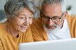 © lashkhidzetim - Elderly couple shares warm smile while looking at laptop screen. They sit close, comfortable, engaged in shared activity. Their expressions show gentle joy and mutual interest