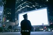 © gankevstock - Security guard watches over a bright billboard in a city at night