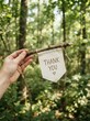© Rincon Studio - Hand holding a thank you banner in a forest setting.