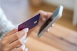 © simona - Woman holding a purple credit card in one hand and a smartphone in the other, making a secure mobile payment and engaging in online shopping or e-commerce from home