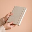 © mdnazirhossain - Person holding a grey planner notebook for planning and scheduling tasks on a solid peach background Mockup