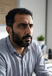 © Pixel-Shot - Serious middle eastern man with beard and furrowed brow looking away in an office setting, this professional portrait captures a moment of contemplation or problem-solving in an office
