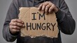 © Arifyape - Person holding cardboard sign with I'm hungry text in poverty concept