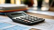 © Thares2020 - A black calculator rests on printed financial documents and papers on a wooden desk surface