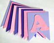 © Yulia Mihaylova - A pastel felt alphabet banner displays the letter A in pink and purple tones. Soft handmade fabric and layered pennants create a charming decoration for a nursery, birthday, or classroom.