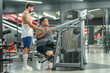 © BESTIMAGE - Disabled friends with prosthetic legs talking and resting in gym inclusive exercising concept. Male and female amputee with artificial limbs discussing workout routine in fitness center.