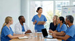 © Xenia - Smiling female nurse leading a medical team meeting in a hospital. Diverse group of doctors and nurses collaborating around a conference table. Healthcare and teamwork concept