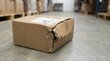 © Xenia - Damaged cardboard package with a crushed and torn corner on a warehouse floor. Broken shipping box in a logistics and distribution center. Delivery problem and mishandled freight concept