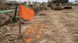 © Xenia - Orange utility locating flag and spray paint marks on dirt. Underground line marking at construction site with trench and machinery