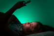 © Volodymyr - Child lying comfortably while using smartphone. Kid browsing online content in bedroom. Child experiencing modern digital bedtime habit. Kid using phone quietly in dark room.
