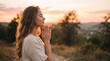 © Finka - A serene woman with long hair praying with hands together in a peaceful outdoor nature setting at sunset