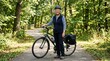 © Sumon - Confident senior woman cyclist with gray hair and blue helmet standing beside her trekking bicycle on a sunny forest path, smiling at camera, lifestyle portrait