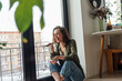 © Westend61 - Cheerful woman with eyes closed sending voicemail through smart phone by glass window at home