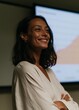 © CYBERPINK - Portrait of a young woman standing in front of a projector screen. she is wearing a white blouse and has shoulder-length dark hair.