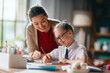 © Konstantin Yuganov - Happy Teacher Helping Young Student with Homework at Home Desk