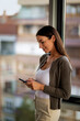 © gzorgz - Smiling businesswoman using phone in a modern office