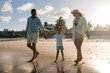 © kleberpicui - Parents walk hand in hand with their young son along a sunny shoreline, splashing in shallow ocean water and enjoying a relaxed summer family vacation filled with laughter and connection.