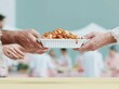 © Ryzhkov - Hands passing a food container over a buttery yellow surface in a clean community kitchen, high-key imagery for charity and meal service