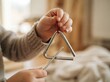 © SimpleDesignStudio - Toddler child playing musical metal triangle instrument indoors close up shot
