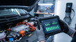© ViskBx - Mechanic holding a diagnostic tablet showing electric vehicle battery health and voltage status in a modern car repair workshop